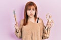 Redhead young woman holding small wooden manikin and painter brushes puffing cheeks with funny face Royalty Free Stock Photo