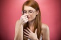 Redhead young woman pinching her nose over pink background