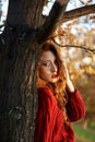 Redhead young woman in a red sweater walks in the park. Autumn beauty portrait of a fashionable Red-haired woman at sunset