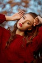 Redhead young woman in a red sweater walks in the park. Autumn beauty portrait of a fashionable Red-haired woman at sunset