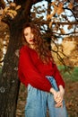 Redhead young woman in a red sweater walks in the park. Autumn beauty portrait of a fashionable Red-haired woman at sunset