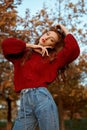 Redhead young woman in a red sweater walks in the park. Autumn beauty portrait of a fashionable Red-haired woman at sunset