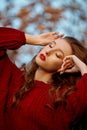 Redhead young woman in a red sweater walks in the park. Autumn beauty portrait of a fashionable Red-haired woman at sunset