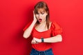 Redhead young woman wearing casual red t shirt looking at the watch time worried, afraid of getting late