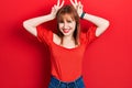 Redhead young woman wearing casual red t shirt posing funny and crazy with fingers on head as bunny ears, smiling cheerful Royalty Free Stock Photo