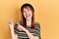 Redhead young woman wearing wool cap smiling and looking at the camera pointing with two hands and fingers to the side Royalty Free Stock Photo