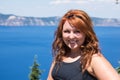 Redheaded female with long hair poses in front of the bright blue lake -Crater Lake Royalty Free Stock Photo