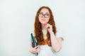 Redheaded woman student in eyeglasses with books in her hand looks thoughtful standing on  white backgroung, learning and Royalty Free Stock Photo