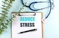 Reduce stress phrase on clipboard with stethoscope, pen and eucalyptus branches on blue background Royalty Free Stock Photo