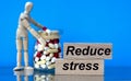 REDUCE STRESS words on a wooden block on a blue background with pills and a wooden man