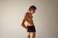 Reduction of back pains. Shirtless young guy with healthy, fit, muscular body standing in underwear against grey studio Royalty Free Stock Photo