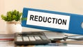 Reduction - blue binder on desk in the office with calculator, pen and green potted plant, concept Royalty Free Stock Photo