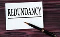 REDUNDANCY - word on a white sheet on a brown wooden background with a pen