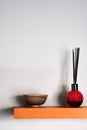 reed diffuser and small bowl on wooden shelf with shadows on wall