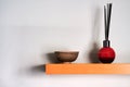 reed diffuser and small bowl on wooden shelf with shadows on wall
