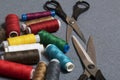 Reels of threads of different colors on a gray woven background. Two pairs of scissors of different sizes.
