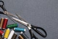 Reels of threads of different colors on a gray woven background. Two pairs of scissors of different sizes.