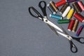 Reels of threads of different colors on a gray woven background. Two pairs of scissors of different sizes.