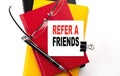 REFER A FRIEND text written on a sticky on colorful notebooks