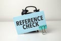 REFERENCE CHECKS is written in a blue sticker near a black alarm clock