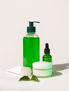 Refillable Cosmetic bottles, jar and tube near green leaves on white, bottles filled with green liquid