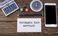 REFINANCE YOUR MORTGAGE written on paper, wooden background desk with calculator, dice, compass, smart phone and pen. Royalty Free Stock Photo