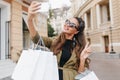 Refined fashionista woman having fun during shopping and making selfie. Outdoor photo of wonderful shopaholic lady Royalty Free Stock Photo