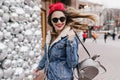 Refined girl in denim jacket posing with trendy backpack on street background. Spectacular woman in Royalty Free Stock Photo