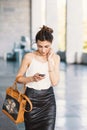 Refined smiling woman walking and writing or reading SMS messages online on a smart phone outdors Royalty Free Stock Photo