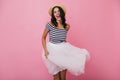 Refined tanned girl with wavy hair playing with her skirt. Indoor shot of slim excited woman in str