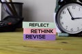 Reflect Rethink Revise. Handwriting on sticky notes in clothes pegs on wooden office desk