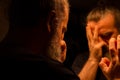 Reflection of bearded man in a dark, holding his head with his hands with painful expression Royalty Free Stock Photo