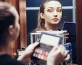 Reflection of a beautiful girl in the mirror doing makeup at the dressing table in the room at home, stylish young woman looking Royalty Free Stock Photo