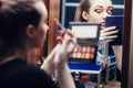 Reflection of a beautiful girl in the mirror doing makeup at the dressing table in the room at home, young woman preparing face, Royalty Free Stock Photo