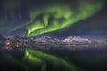 Reflection of the beautiful northern lights in he water surrounded by snow covered mountains