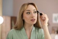 Reflection of beautiful woman applying mascara in mirror at home Royalty Free Stock Photo