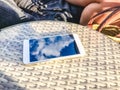 Reflection of blue sky with clouds in the phone-smartphone, which lies on a bright wicker table against the background. Blur and Royalty Free Stock Photo