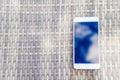 Reflection of blue sky with clouds in the phone-smartphone, which lies on a bright wicker table against the background. Blur and Royalty Free Stock Photo