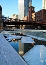 Reflection of buildings in water while bridge spans a frozen Chicago River with ice chunks. Royalty Free Stock Photo