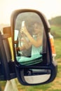 Reflection in a camper van rear-view mirror of a woman taking a picture with her mobile