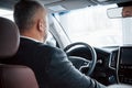 Reflection of face in the front mirror. View from behind of senior businessman in official clothes driving a modern new