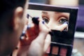 Reflection of a female eye in a palette mirror with multi-colored shadows, girl doing makeup indoors, drawing an arrow on the