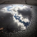 Reflection of fluffy clouds in a shallow puddle on a paved surface Royalty Free Stock Photo