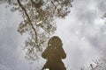 Reflection of a girl in a jacket with a hood in a puddle of water with trees on the background. A girl make photo in the puddle. A Royalty Free Stock Photo