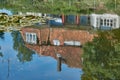 Reflection of a house with red roof tiles and a green tree on the surface of a pond with water lily leaves Royalty Free Stock Photo