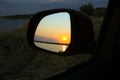 Reflection of landscape with beautiful sunset over calm river in car side view mirror, closeup Royalty Free Stock Photo