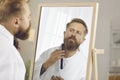 Reflection in mirror of handsome man combing his beard in preparation for work or important event.