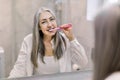 Reflection in the mirror of smiling beautiful senior lady with long straight gray hair, standing in bathroom, brushing Royalty Free Stock Photo