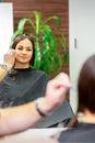 Reflection in the mirror of the young caucasian woman sitting and receiving haircut by male hairdresser at hairdresser Royalty Free Stock Photo