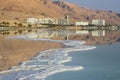 Reflection of mountains, hotels and palm trees in the water of the Dead Sea with salt formations Royalty Free Stock Photo